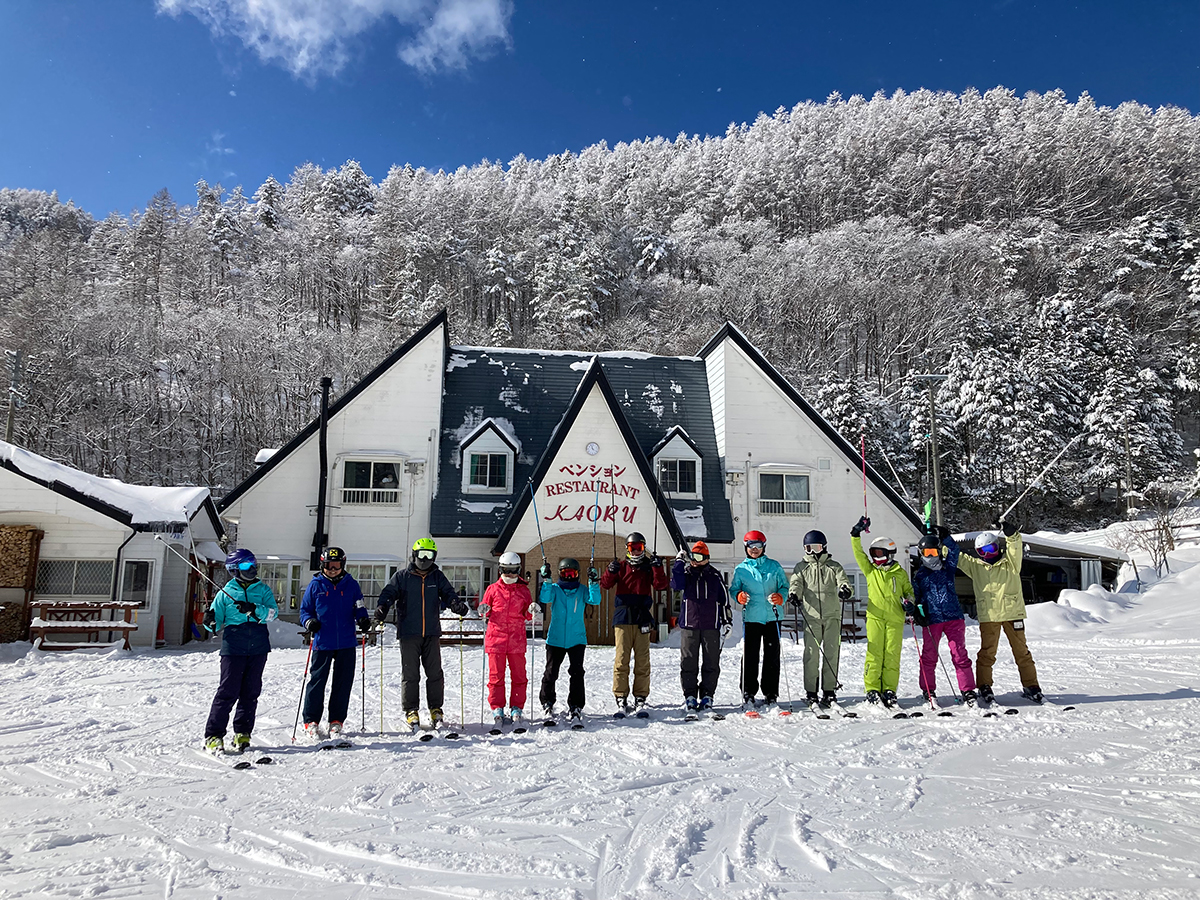 青空と樹氷の山を背にペンションかおるの前に並ぶスキーヤーたち