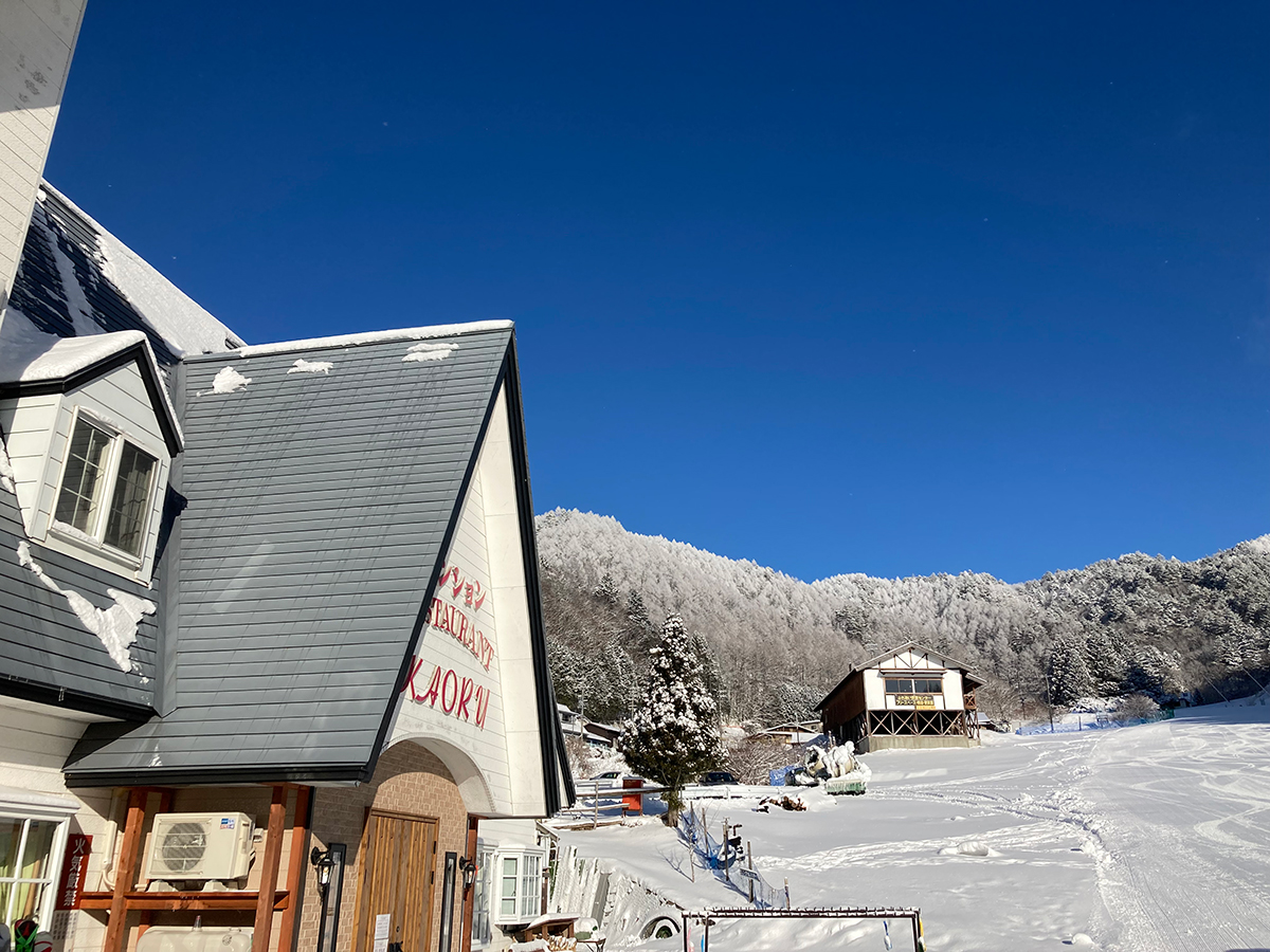 雪をかぶったペンションかおるの屋根と青空のゲレンデ